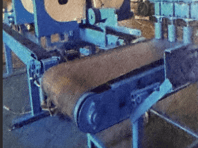 Blue industrial bandsaw with conveyor belt and control panel in workshop setting.