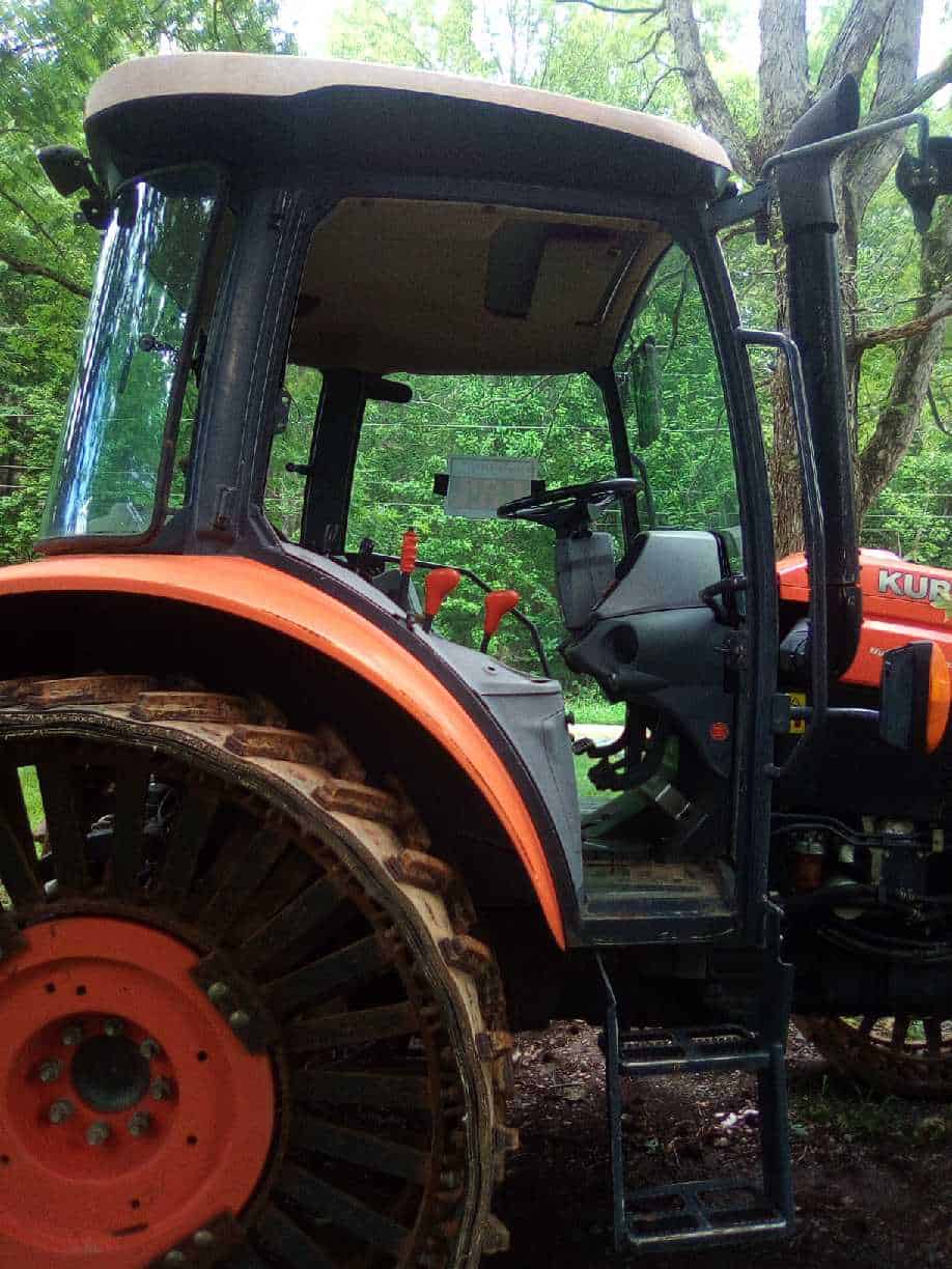 image000001 (5) 2018 Kubota M5-111 tractor with enclosed cab and large rear tires in a wooded area.