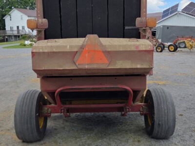 Heavy-duty dump trailer with black bed and red frame, large rear wheels, and orange reflective triangle.