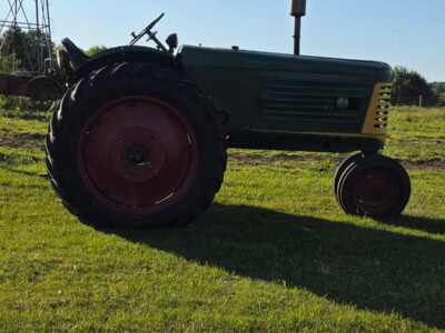 Oliver 77 tractor with green body and red wheels on grassy field under clear sky.