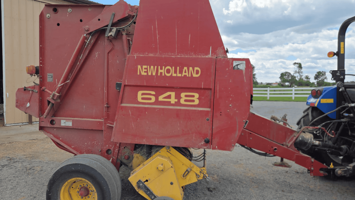 New Holland 648 round baler in red with yellow wheels and branding.