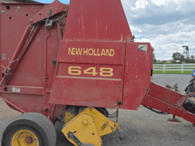 New Holland 648 round baler in red with yellow wheels and branding.