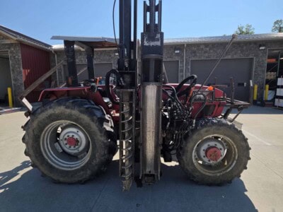 Red Log Cabin Pro tractor with forklift attachment and large tires.