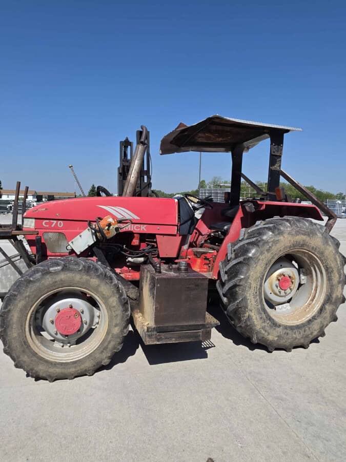 Red McCormick C70 tractor with canopy and large tires on a farm lot.