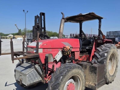 Red agricultural tractor with canopy, large tires, and front weight attachment on a concrete lot under blue sky.