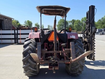Red agricultural tractor with canopy, large tires, and front loader attachment on a concrete lot.