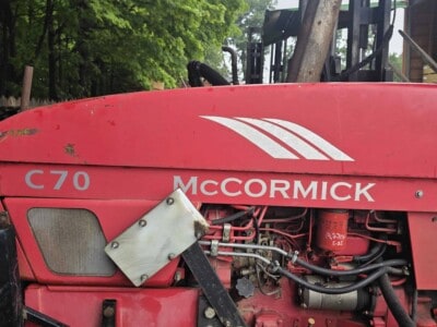 Red McCormick C70 tractor with visible engine and tracks, outdoor setting with trees in background.