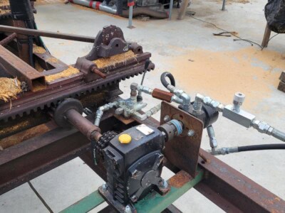 Close-up of hydraulic pump and piping on sawmill machinery in outdoor yard.