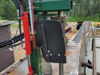 Close-up of green industrial sawmill with safety guards and hydraulic controls.