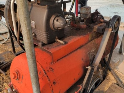 Vintage industrial air compressor with black motor and orange tank, used for powering pneumatic tools.
