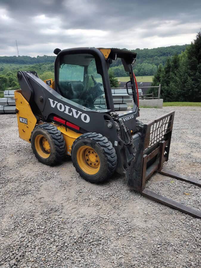 2019 Volvo MC85C skid steer loader with enclosed cab and fork attachment on gravel surface.