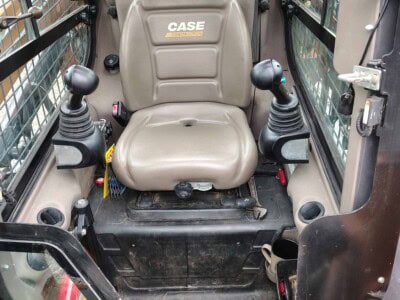 CASE construction equipment cab with beige seat and control joysticks.