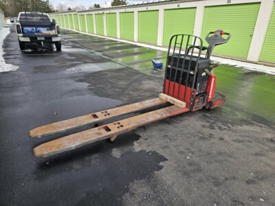 2006 Raymond 8400 electric pallet jack with worn forks and control handle on wet asphalt.