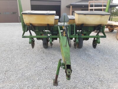 John Deere 7000 planter with dual seed hoppers and row units, green frame, on gravel surface.