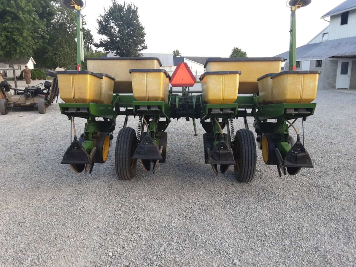 John Deere 7000 planter with yellow seed hoppers and black row units on gravel surface.