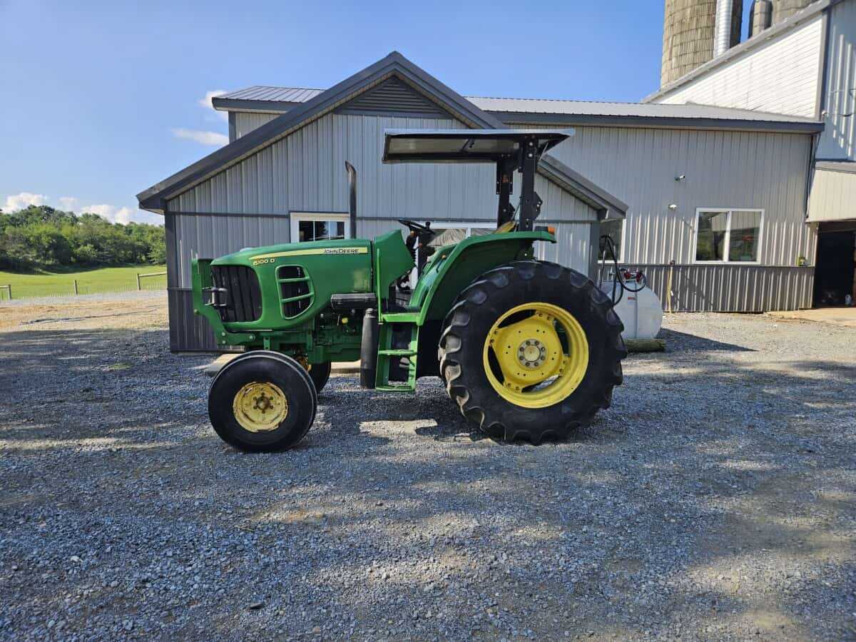 Green John Deere 6100D tractor with cab and large rear tires on gravel surface.