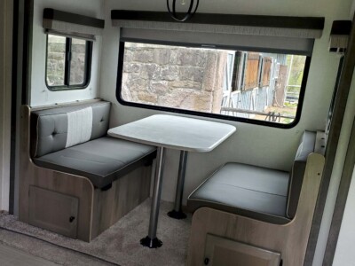 RV interior with dinette and large window, modern decor, and built-in storage.