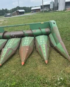 John Deere 6-Row All-Crop Head with green and rusted metal, visible cutting bars and attachment points.