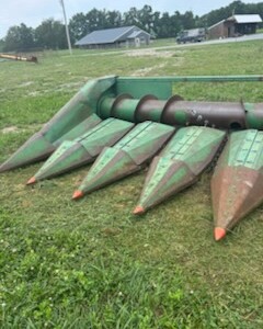 John Deere 6-Row All-Crop Head with green paint and rusted metal parts on a farm field.