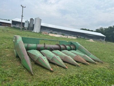 Green John Deere 6-Row All-Crop Head with worn blades on grassy field.