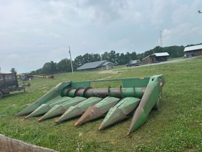 Green John Deere 6-Row All-Crop Head with sharp points and rollers on grassy field.