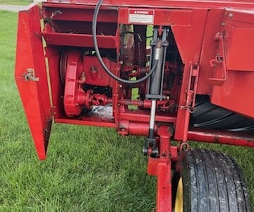 Red New Holland 1465 Haybine with hydraulic components and large tires on grassy field.