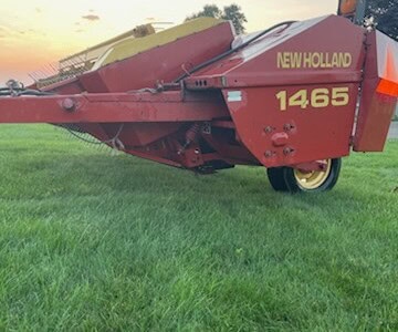 New Holland 1465 haybine in red with yellow branding on green field at sunset.
