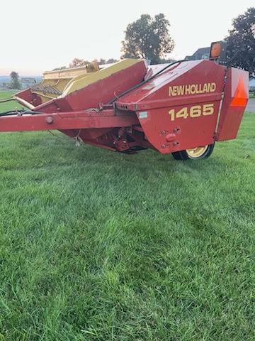 New Holland 1465 haybine with red body and yellow cutting reel on green field.