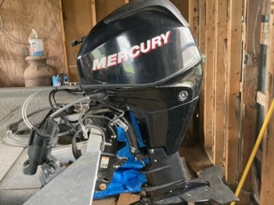 Black Mercury outboard motor with red and white logo, mounted on boat in a workshop setting.