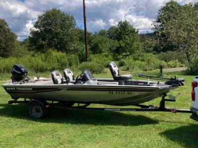 Bass Tracker fishing boat with three outboard motors on a trailer in a grassy field.