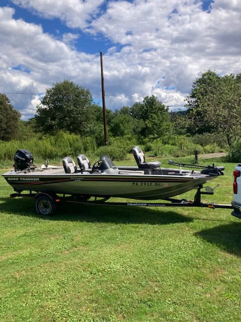 Bass Tracker fishing boat with three outboard motors on a trailer in a grassy field.