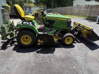 John Deere X738 lawn tractor with front blade attachment and yellow seat.