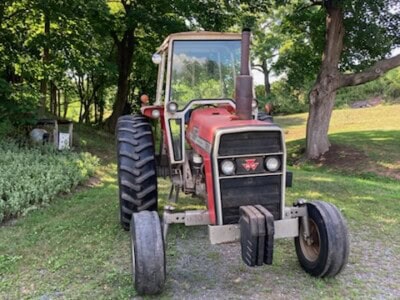 Red Massey Ferguson 285 tractor with enclosed cab and front weight in a grassy area with trees.