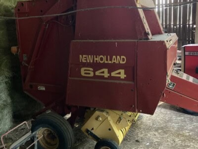 Red New Holland 644 round baler with yellow pickup and black wheels in barn.