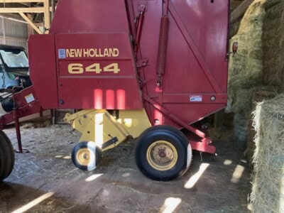 Red New Holland 644 round baler in barn with hay bales nearby.