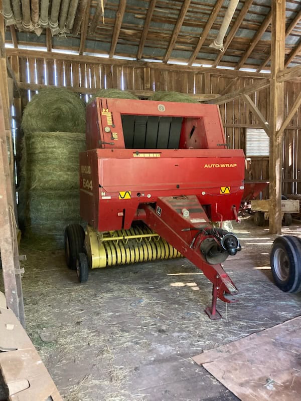 Red Auto-Wrap hay baler with yellow pickup in a barn setting.