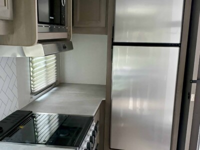RV kitchen with stainless steel refrigerator, microwave, stove, and cabinetry.