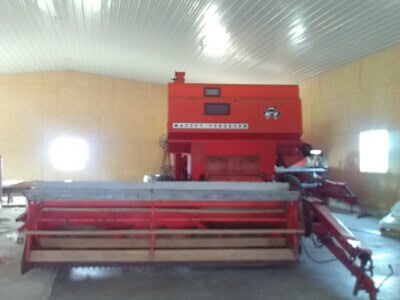 Red agricultural equipment with large cutting attachment inside storage building.