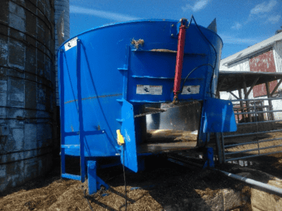 Blue stationary TMR mixer with hydraulic lift and mixing chamber, used in livestock feed preparation.