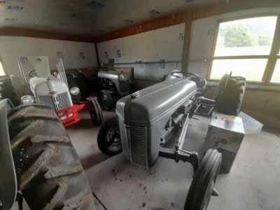 Collection of vintage tractors including a gray tractor with large rear wheels inside a barn.