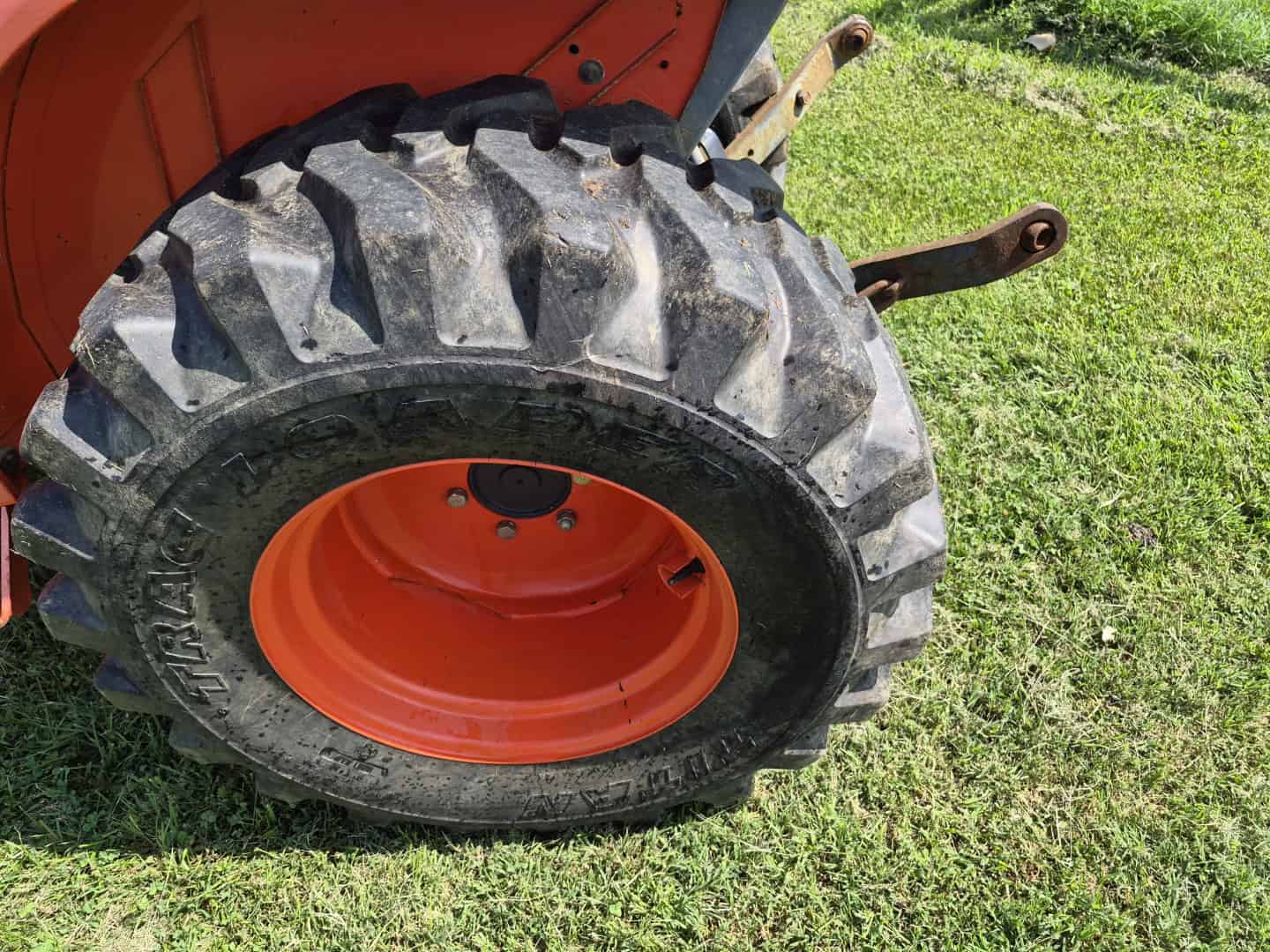 Resized_20260720_152908 Close-up of large tractor tire with orange rim on grassy field.