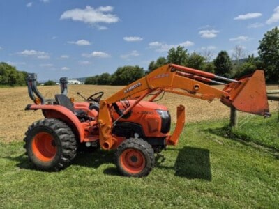 Kubota L3800D compact tractor with front loader, orange color, large rear tires, and enclosed cab, on grassy field.