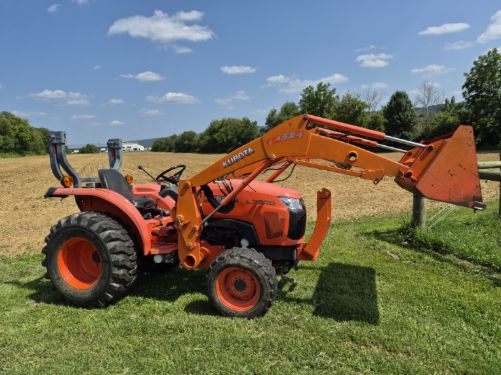 Kubota L3800D compact tractor with front loader, orange color, large rear tires, and enclosed cab, on grassy field.