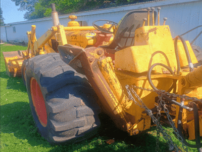 Yellow construction tractor with large rear tires and front loader attachment on grassy area.