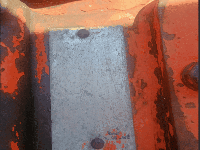 Close-up of a metal plate on orange construction equipment with visible rust and wear.