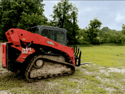 2016 Kubota SVL95-2 compact track loader with enclosed cab and rubber tracks on grassy terrain.