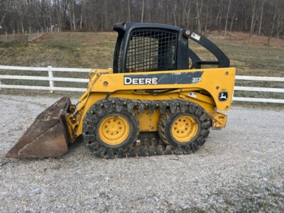 John Deere 317 compact skid steer loader with bucket attachment and enclosed cab.