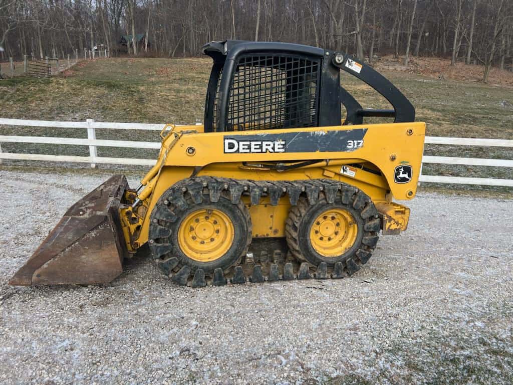 John Deere 317 compact skid steer loader with bucket attachment and enclosed cab.
