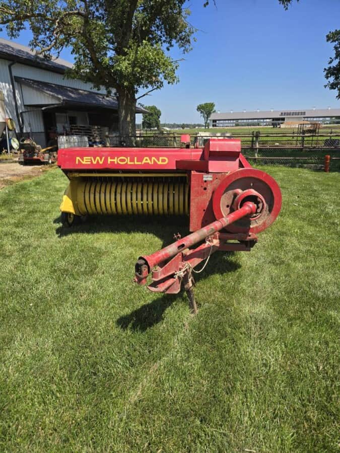 New Holland 273 hay rake with red and yellow color, large wheels, and tines for hay collection.