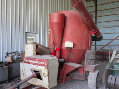 International 1150 grain auger with red hopper and long discharge tube inside a storage shed.
